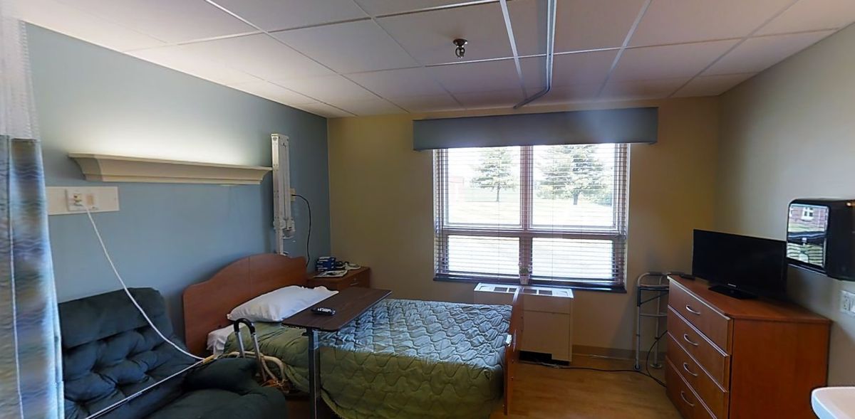 A clean and well-lit hospital room with a single bed and large windows.