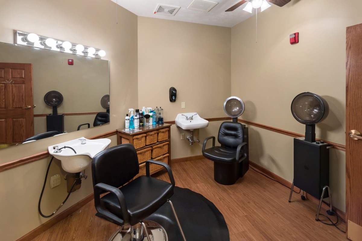 A cozy hair salon interior with styling chairs, a mirror, sink, and hair products on display.