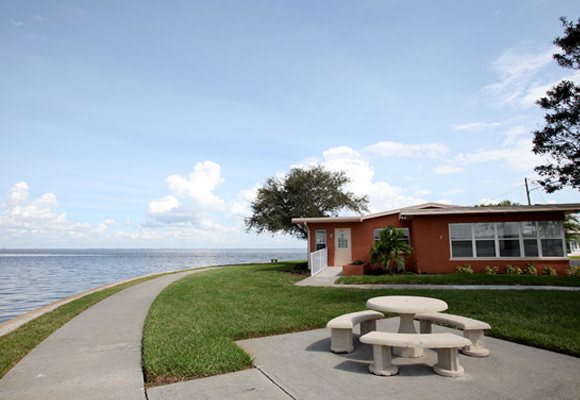 A waterfront house with a nearby picnic table and sidewalk overlooking a lake.