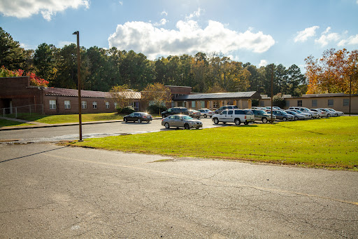A view of a building surrounded by a parking lot, with vehicles parked and green grass in the foreground.