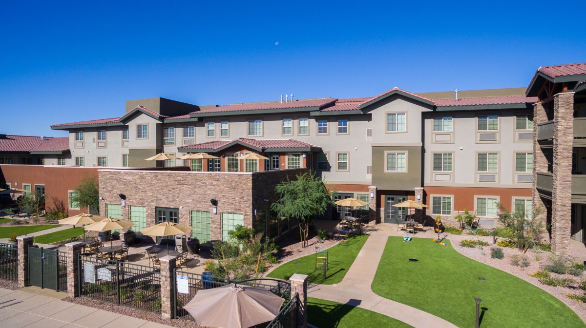 A residential apartment complex with a green lawn and outdoor seating area.