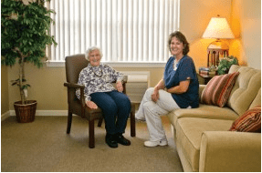 An elderly woman sitting with a caretaker in a cozy living room.