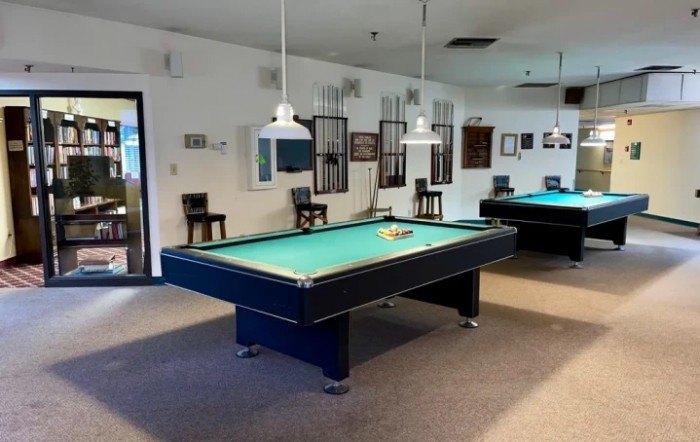 A spacious game room featuring pool tables and overhead lighting.