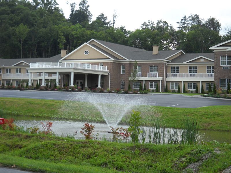 A scenic view of a large building with a fountain in the foreground, surrounded by greenery.