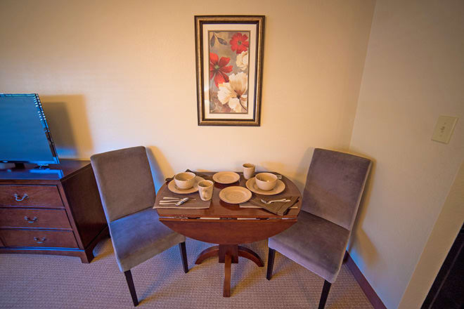 A cozy dining nook with a round table set for two and artwork on the wall.
