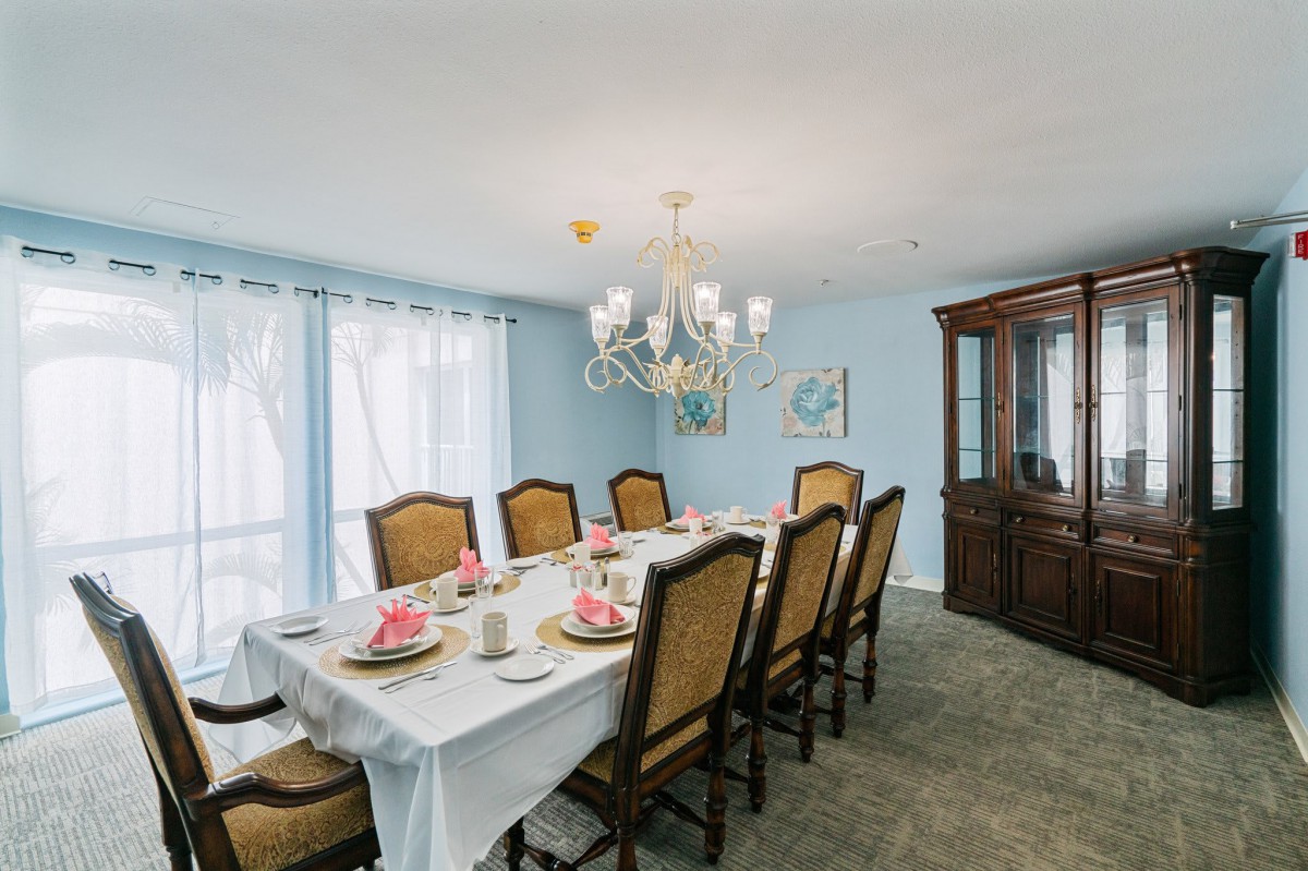 A formal dining room with a long table set for guests, featuring elegant chairs and a chandelier.