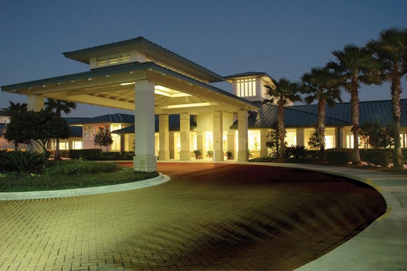 A well-lit building entrance at night with palm trees and modern architecture.