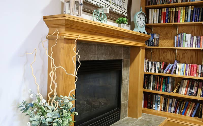 A cozy living room corner featuring a wooden fireplace mantel adorned with decorative items and surrounded by bookshelves.