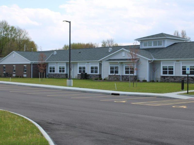 A single-story building with a sloped roof and a neatly maintained lawn in front, adjacent to a paved road.