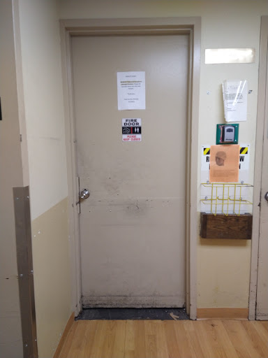 A view of a door in a hallway with various notices attached.