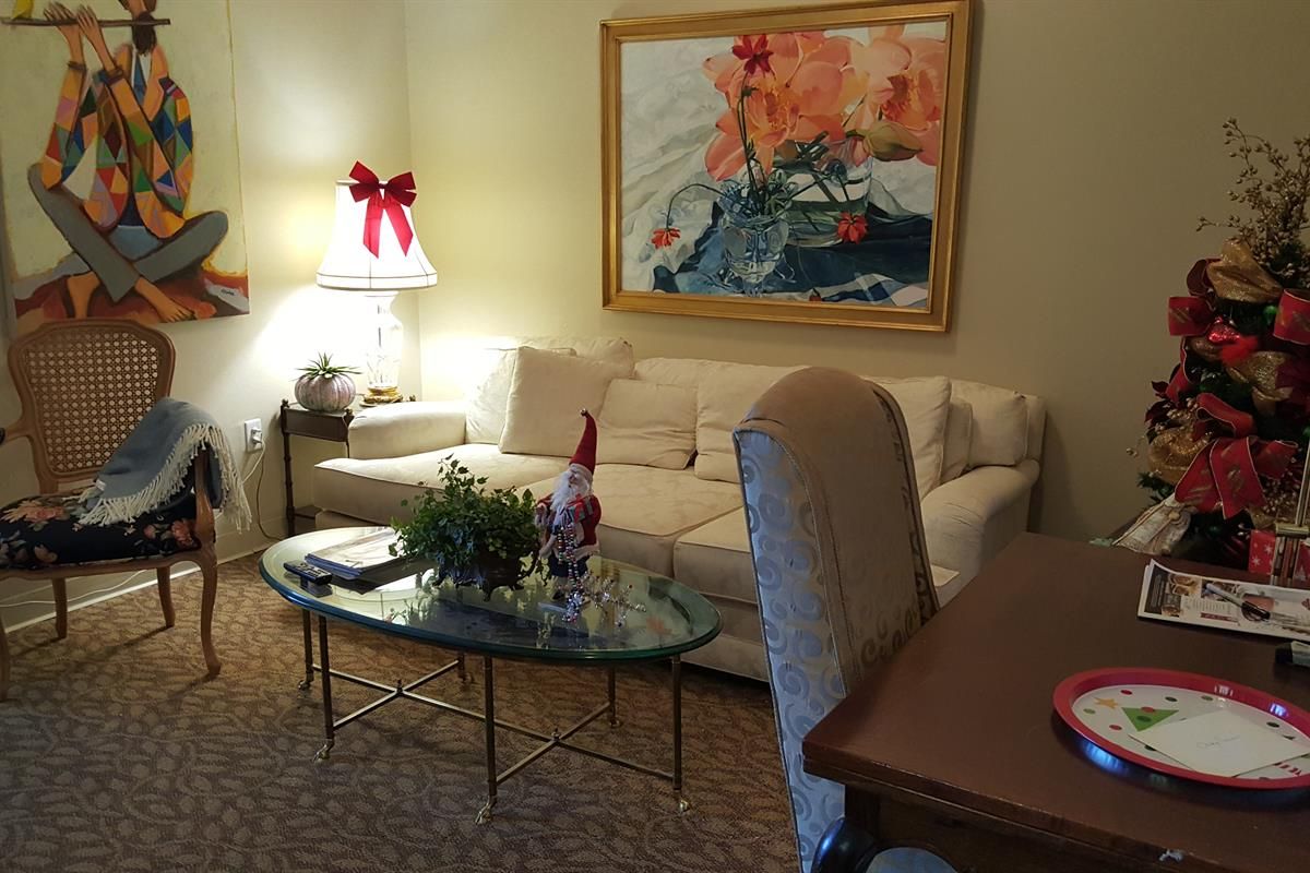 A cozy living room with holiday decorations, featuring a sofa, glass coffee table, and vibrant artwork on the wall.