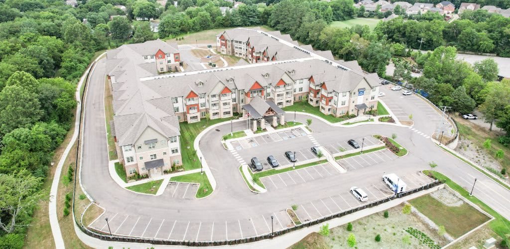 Aerial view of a residential complex with multiple buildings and a parking area surrounded by trees.