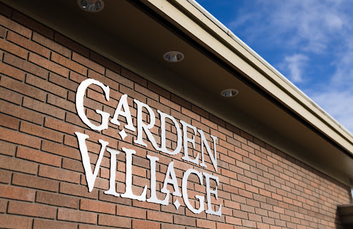 A close-up view of the 'Garden Village' sign displayed on a brick wall.