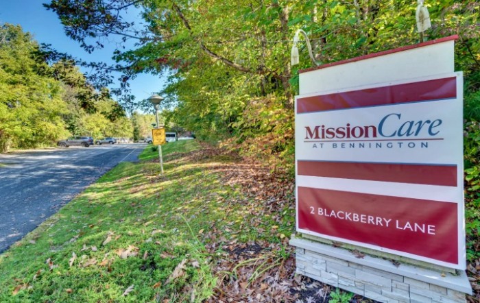 Sign for Mission Crossing Apartments located by a roadside with trees.