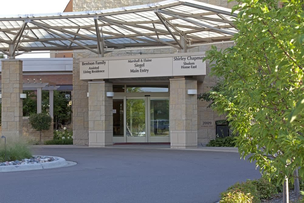 Entrance to a hospital building with visible signs for various departments.