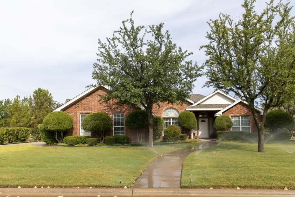 A suburban brick house with a well-maintained front yard and trees.