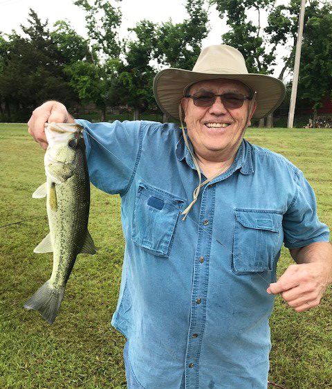 A person smiling while holding a fish outdoors.