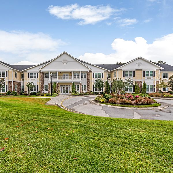 A large residential building with manicured lawns and a circular driveway under a partly cloudy sky.