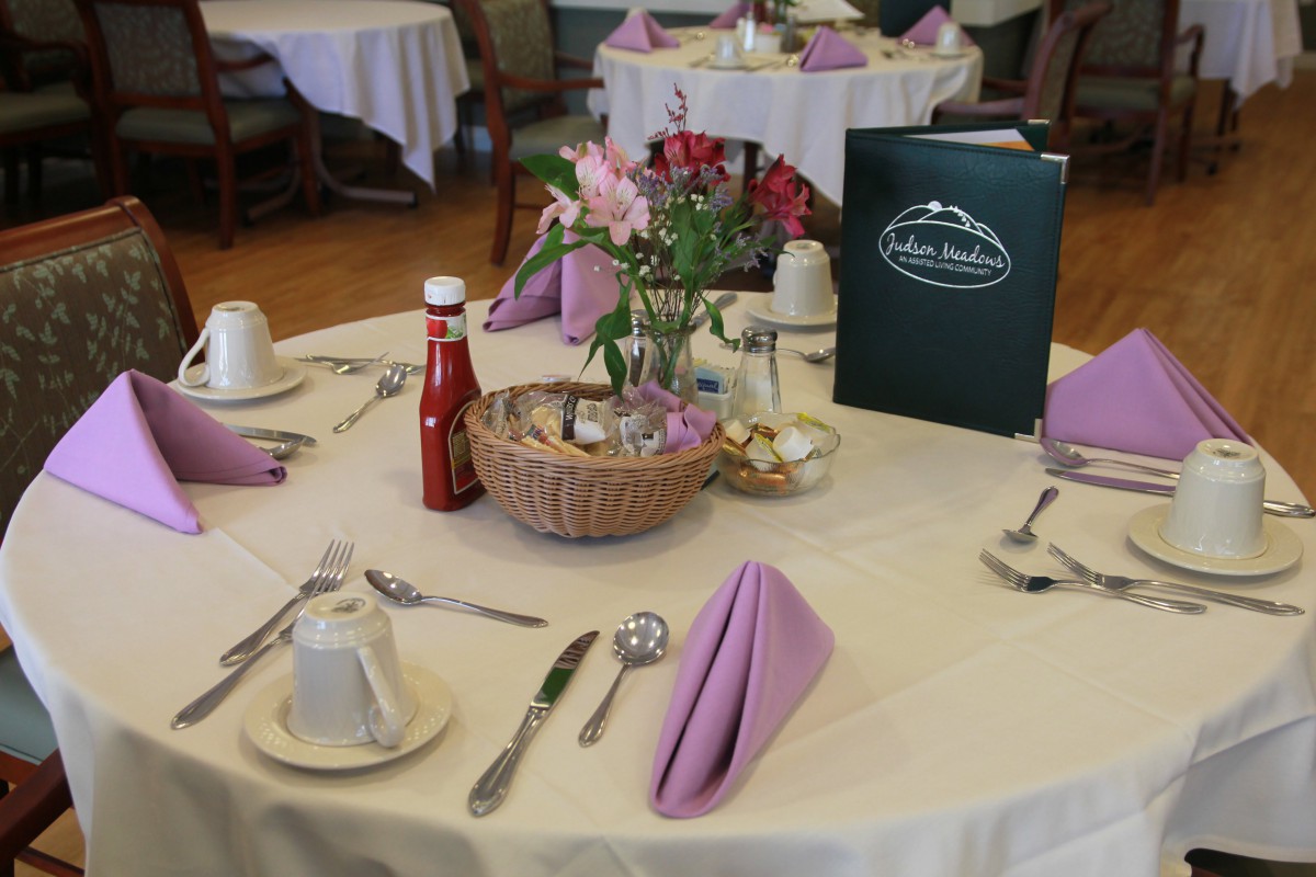 A neatly set dining table with purple napkins, a menu, and floral centerpiece.