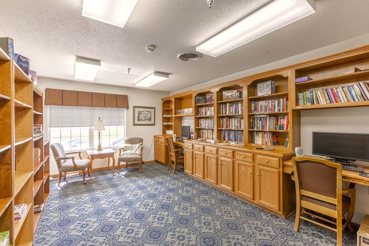 A well-lit library room with bookshelves, a desk, and comfortable seating.