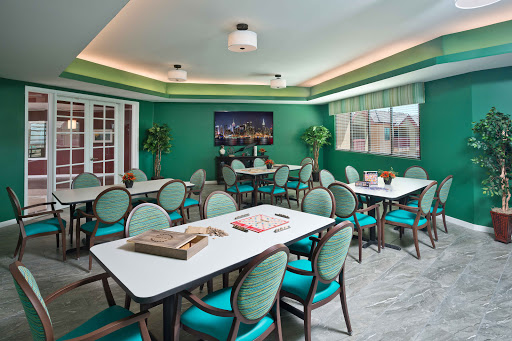A vibrant and inviting fitness center room featuring modern tables and chairs, surrounded by green walls and decorative plants.