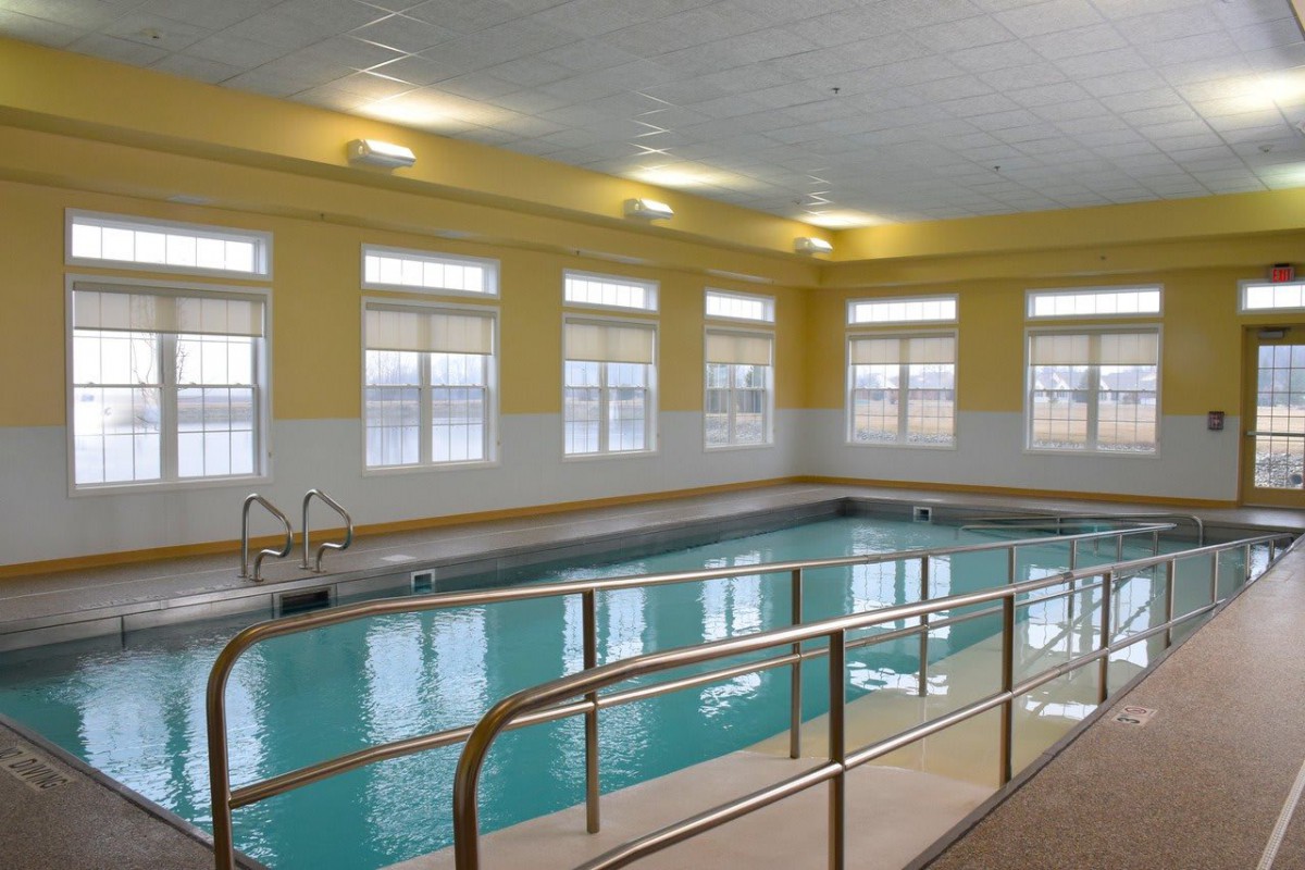 A bright indoor swimming pool area with surrounding windows and safety railings.