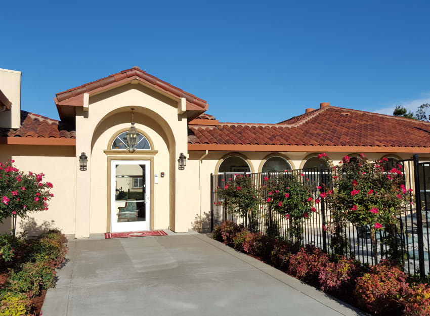 A sunny view of a one-story house with a red-tiled roof and gated entrance.