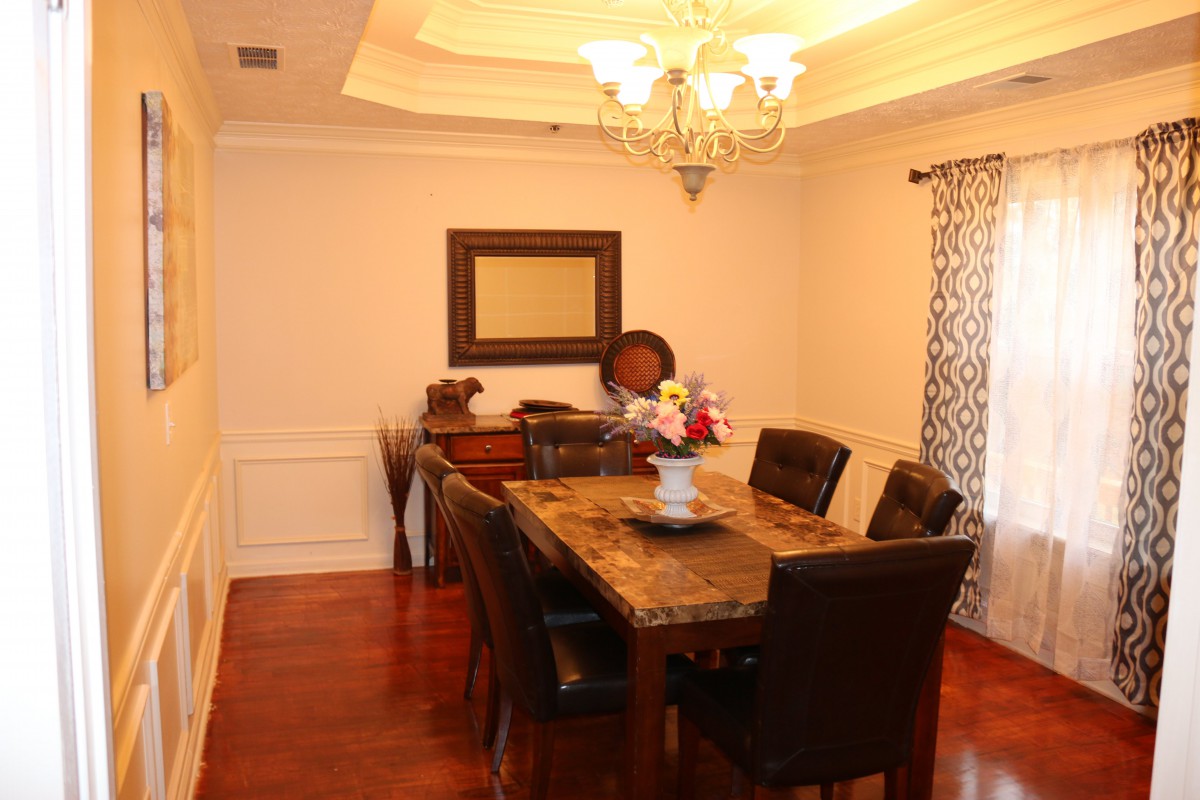 A well-furnished dining room with a central table, surrounded by chairs and illuminated by a chandelier.