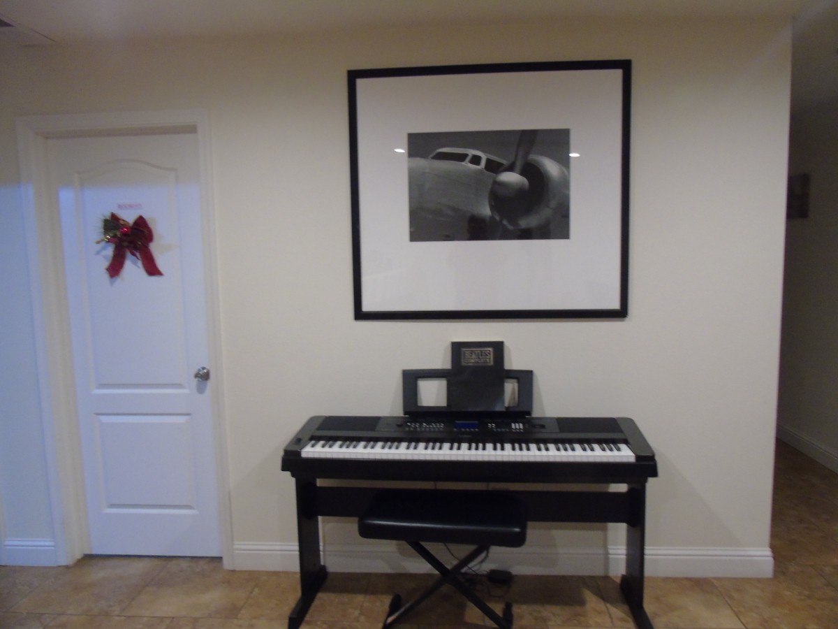 A piano keyboard is positioned against a wall, accompanied by a framed photograph hanging above it.