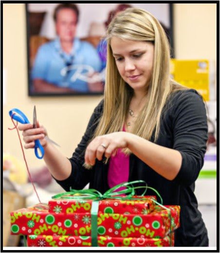 A woman carefully wrapping a gift with colorful paper and ribbon.