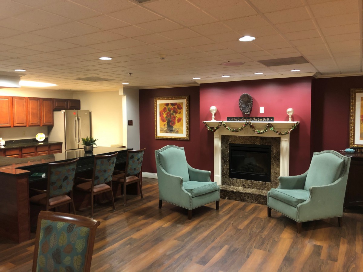 A cozy living room with armchairs around a fireplace, featuring warm decor and wood flooring.