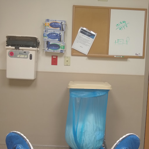 A view of a hospital waiting area with a blue trash can and a bulletin board.
