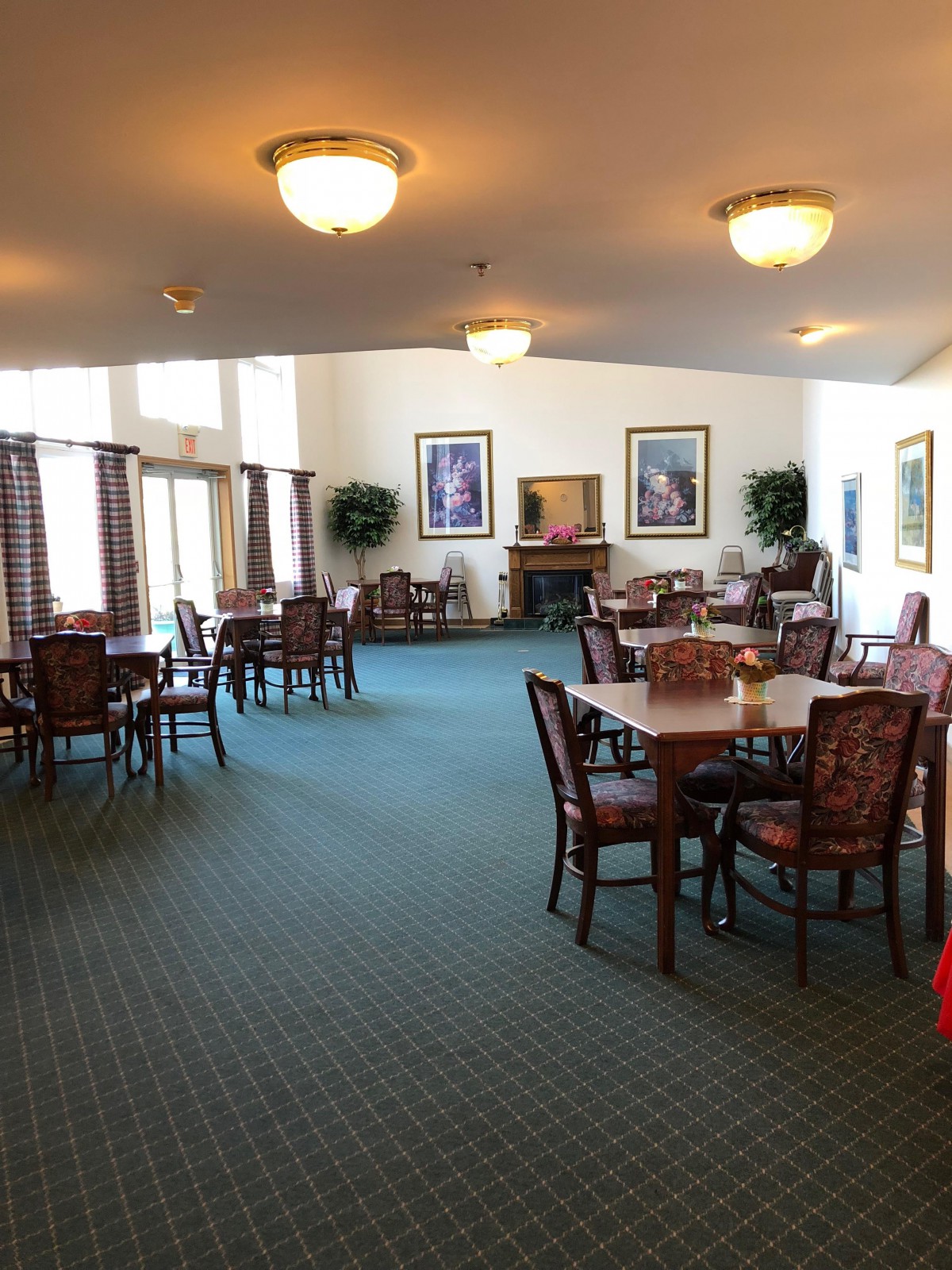 A spacious dining area with neatly arranged tables and chairs, featuring warm lighting and artwork on the walls.