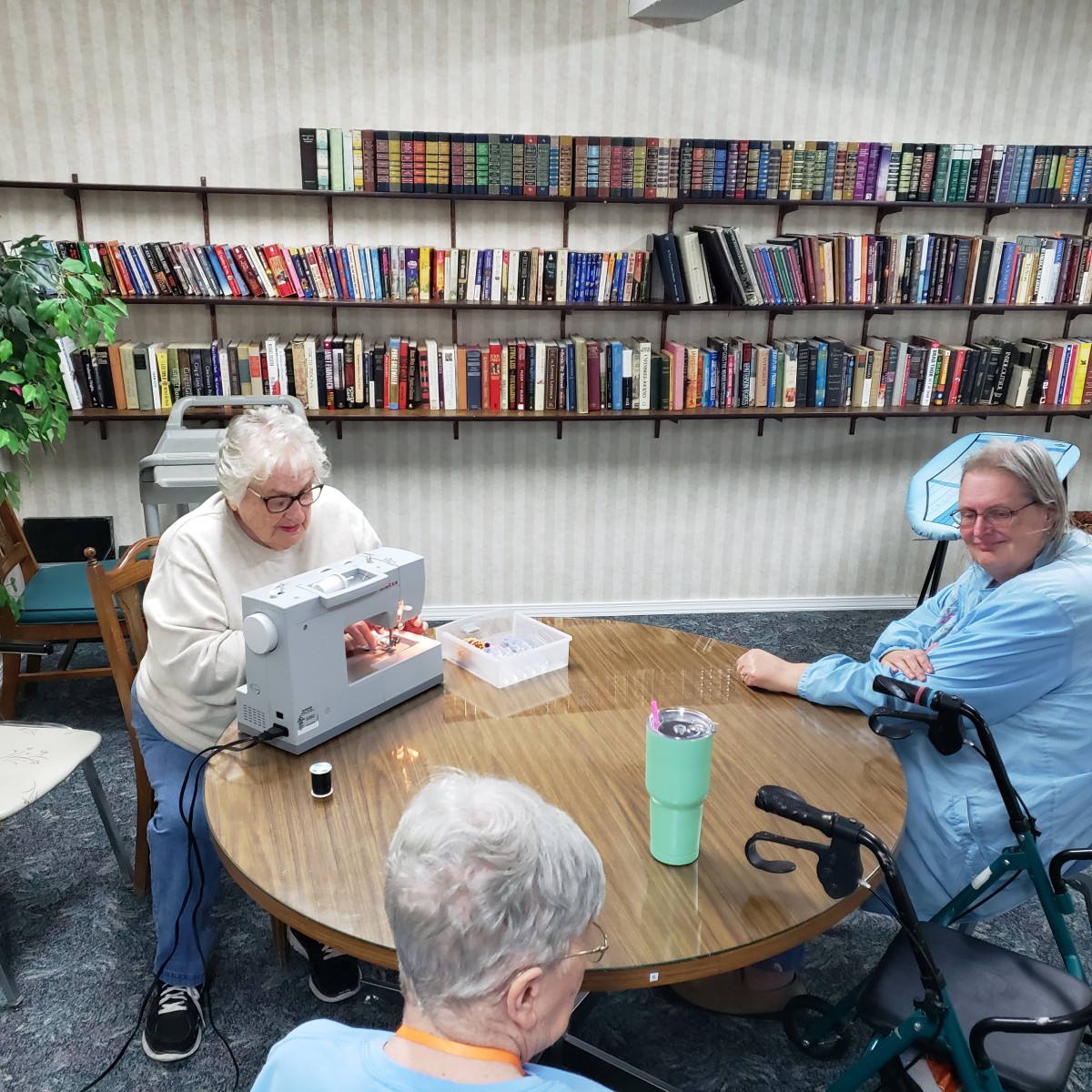 A group of seniors gathered around a table in a library, with one person working on a sewing machine.