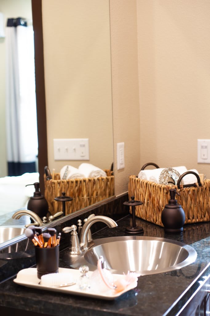 A neatly organized bathroom countertop with a stainless steel sink, faucet, and a wicker basket holding towels and toiletries.