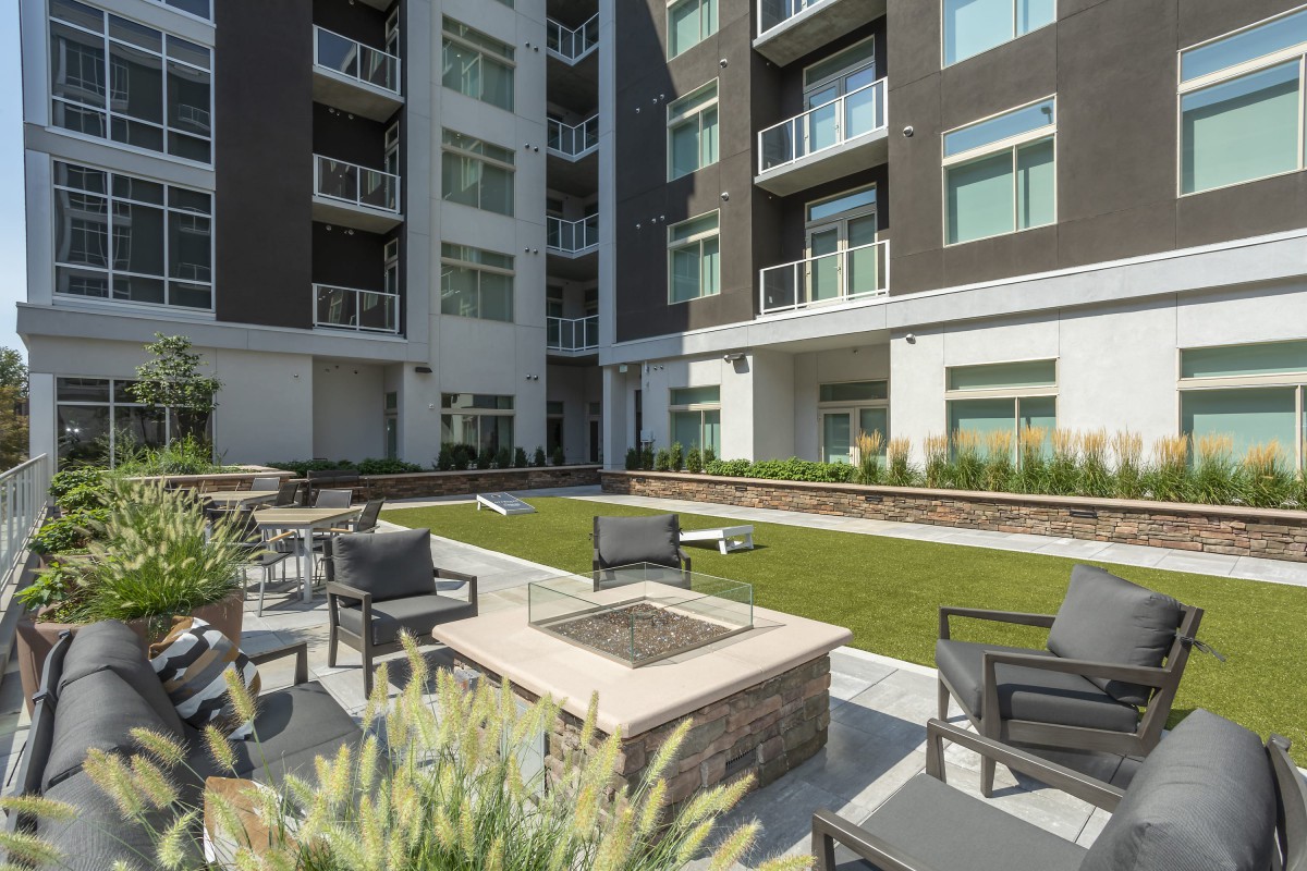 A modern apartment complex features an inviting outdoor seating area with a fire pit and well-maintained landscaping.