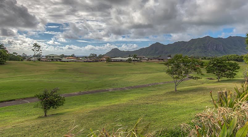 A scenic view of lush green fields with mountains in the background under a cloudy sky.