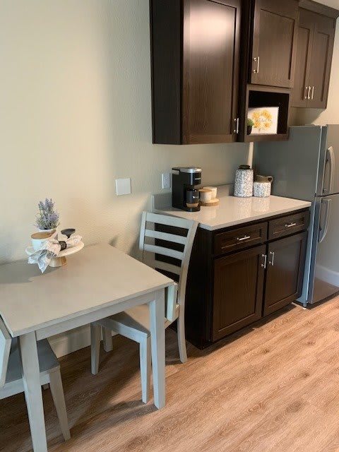 Small kitchen area with a table and chairs, dark cabinets, and appliances including a fridge and coffee maker.