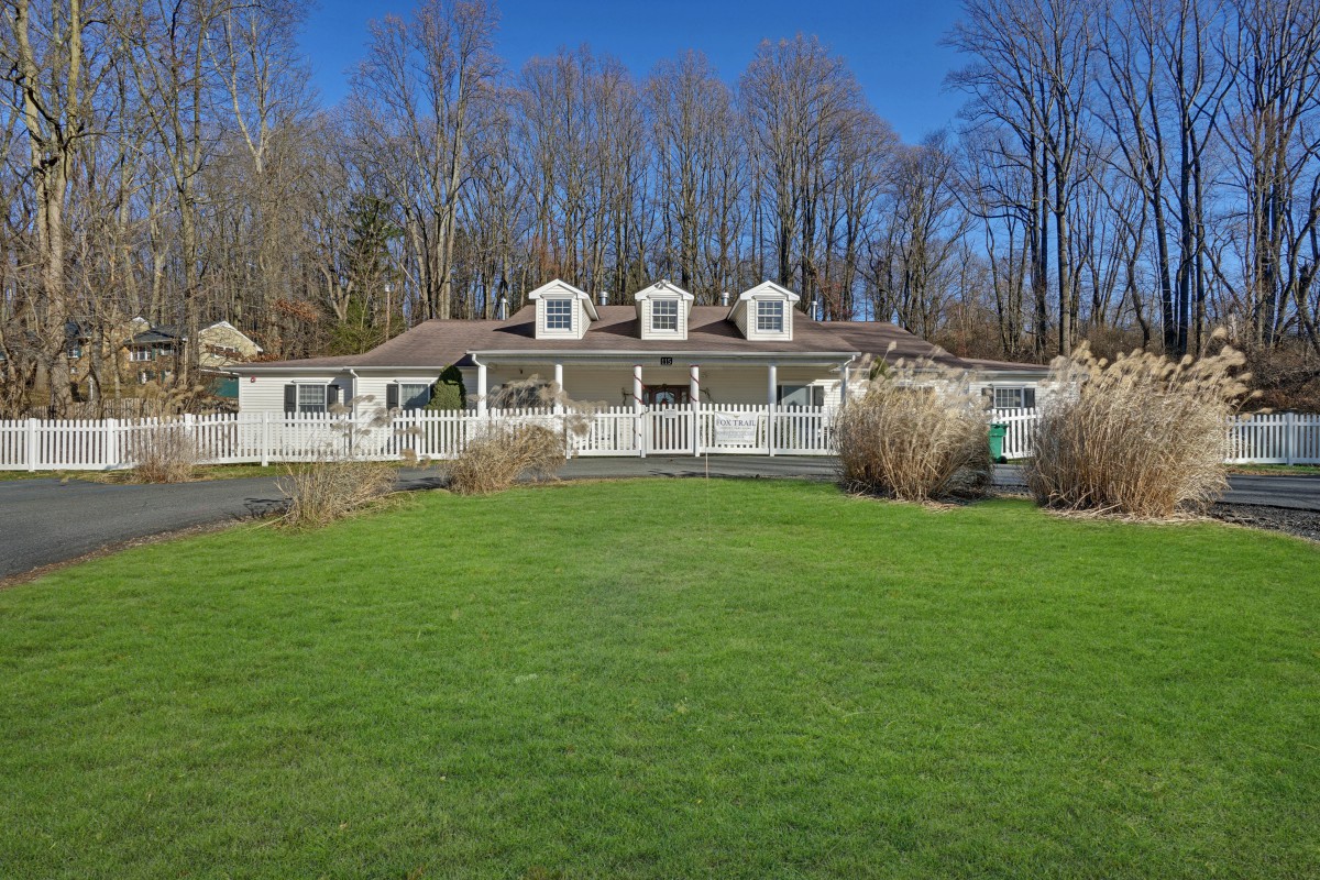 A charming house with a large lawn and trees in the background under a clear blue sky.