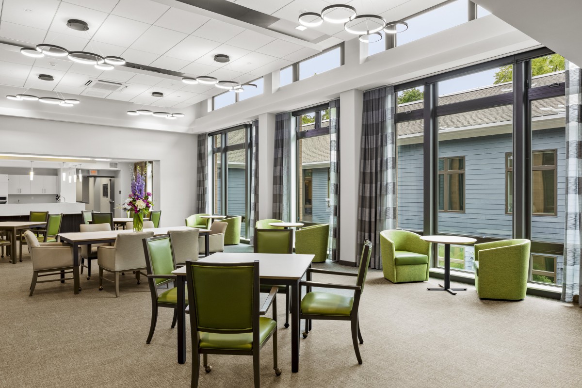A modern dining area with green chairs, large windows, and ample natural light.