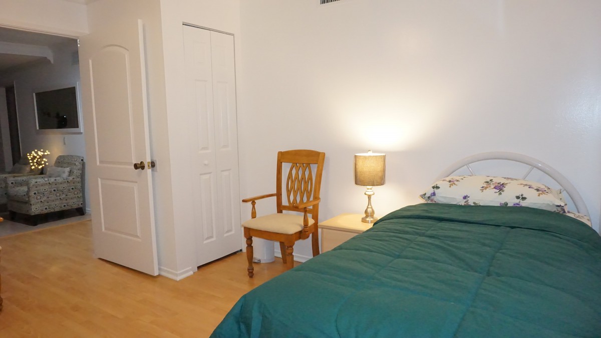 A cozy bedroom featuring a bed with a green duvet, a wooden chair, and a nightstand with a lamp.