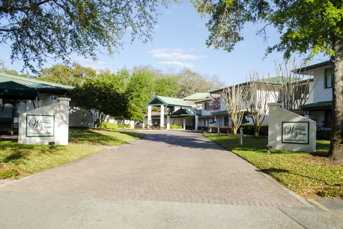 A scenic view of a building with a driveway surrounded by trees under a clear sky.
