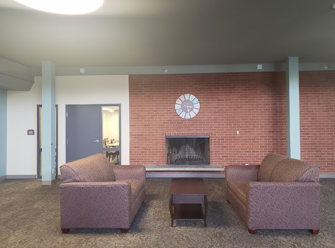 Cozy lounge area with two couches facing a brick fireplace and a clock on the wall.