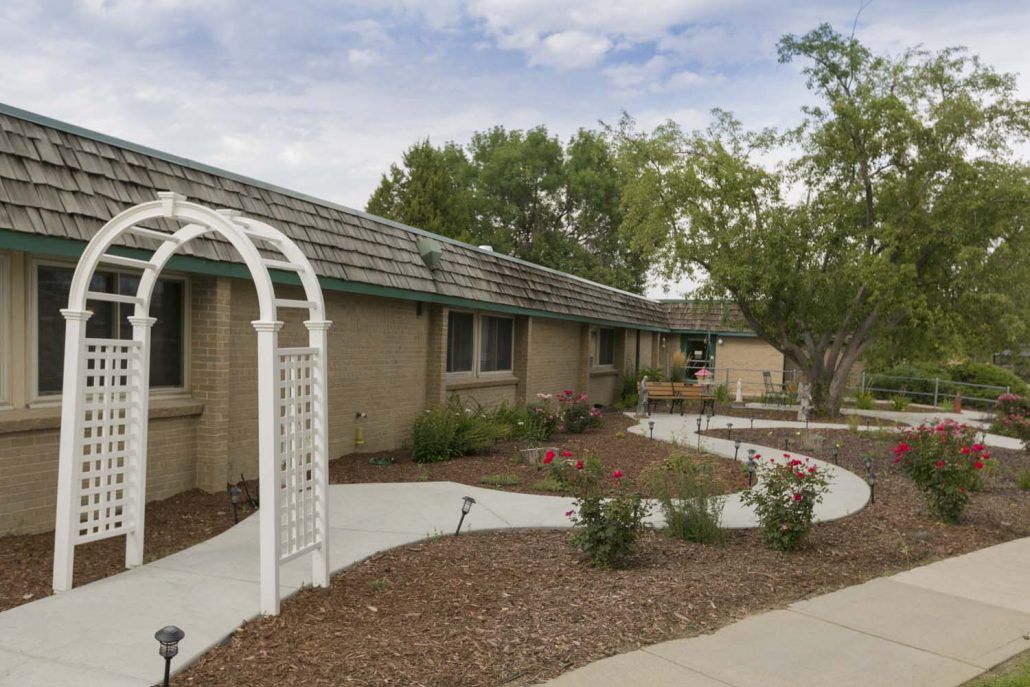 A single-story house with a landscaped garden and pathway featuring an arched trellis.