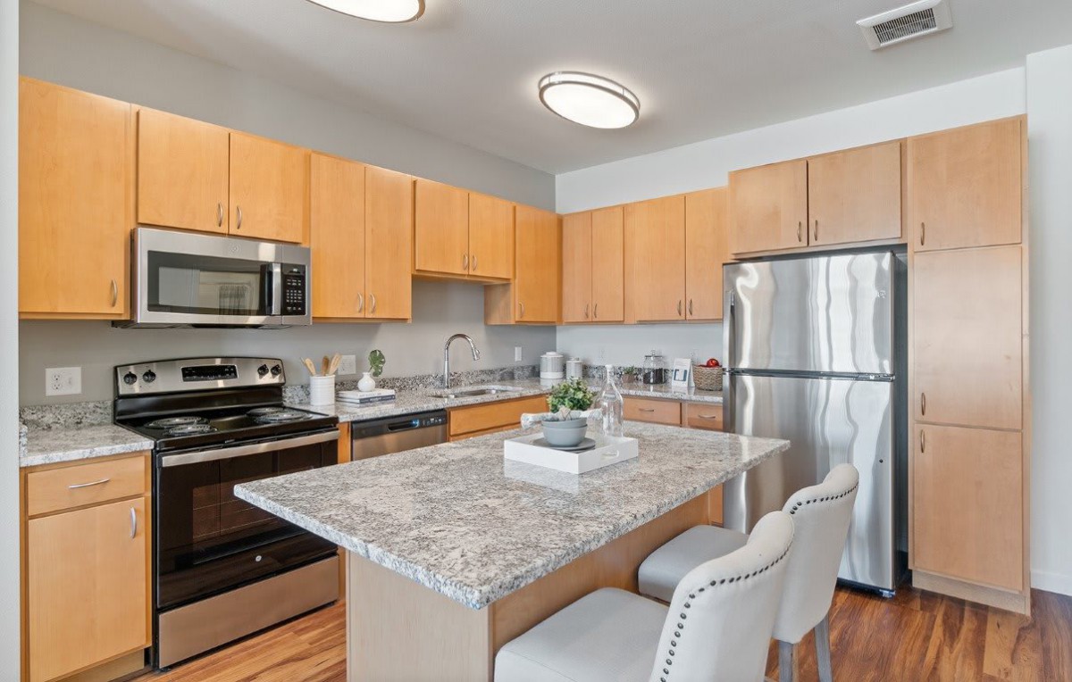 A modern kitchen with stainless steel appliances, a granite countertop island, and wooden cabinets.