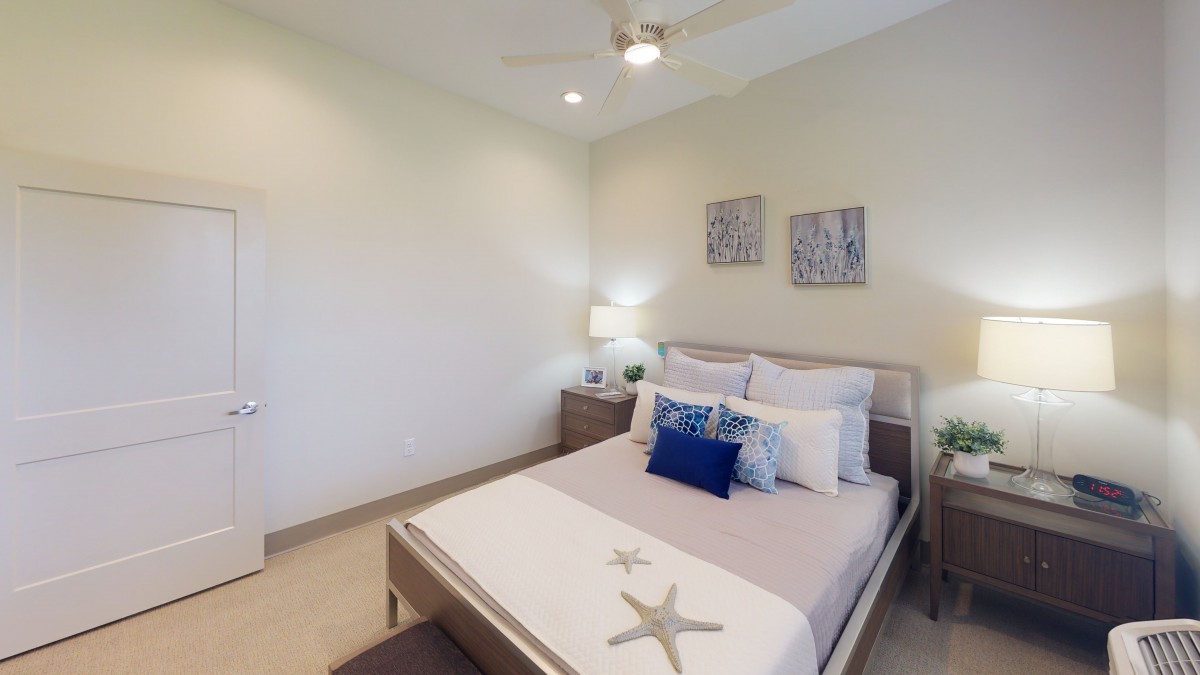 A modern bedroom featuring a neatly made bed with decorative pillows, a nightstand with a lamp, and two pieces of artwork on the wall.