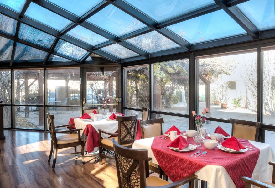 A brightly lit restaurant with elegant table settings under a glass roof.