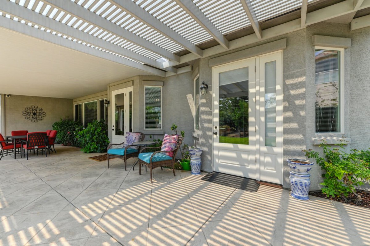 A cozy outdoor patio area with chairs and a table under a pergola casting shadows.