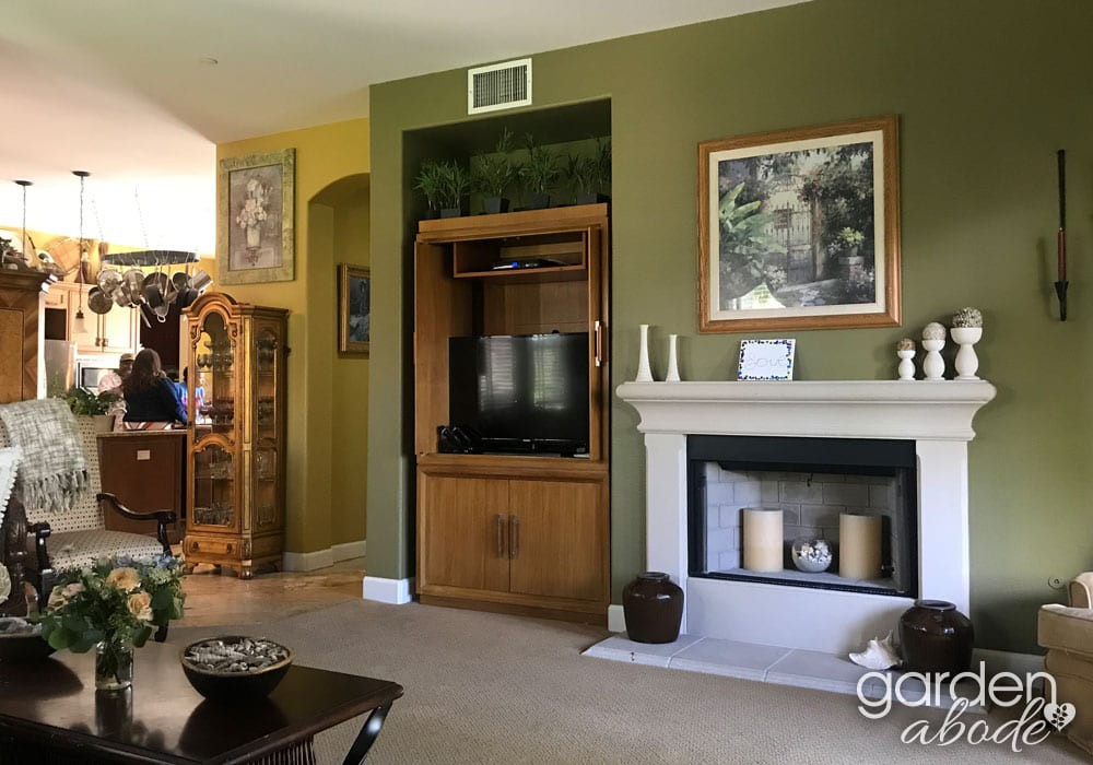 A cozy living room with green walls features a fireplace, a television housed in a wooden cabinet, and various decorative items.