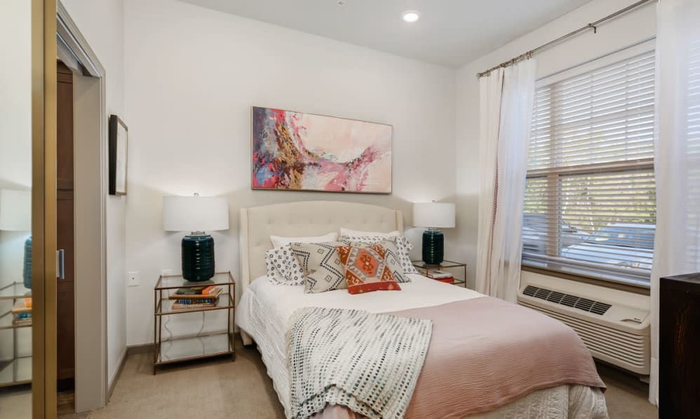 A modern bedroom with a comfortable bed, decorative pillows, abstract artwork above the headboard, and side tables with lamps.